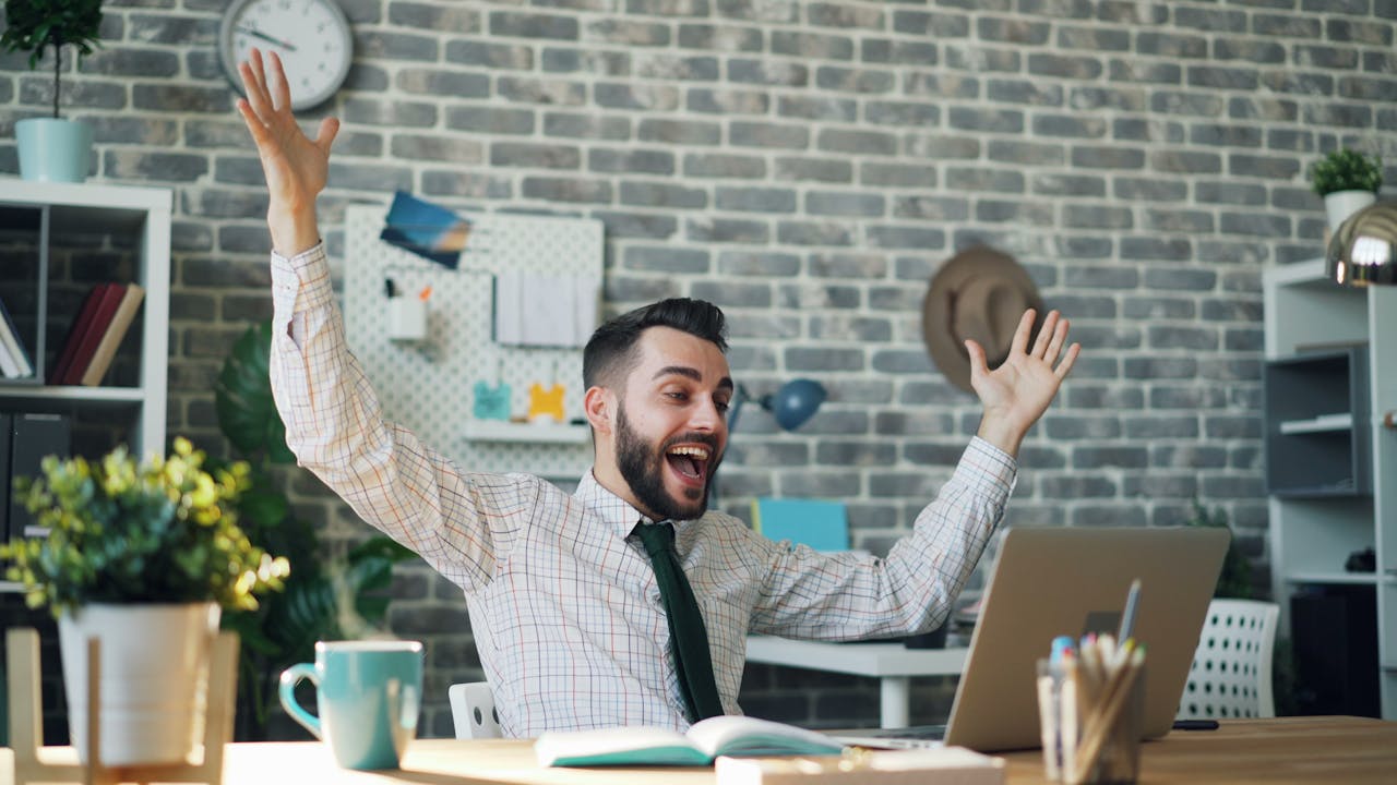 A delighted office worker celebrating success at his desk in a modern office setting.